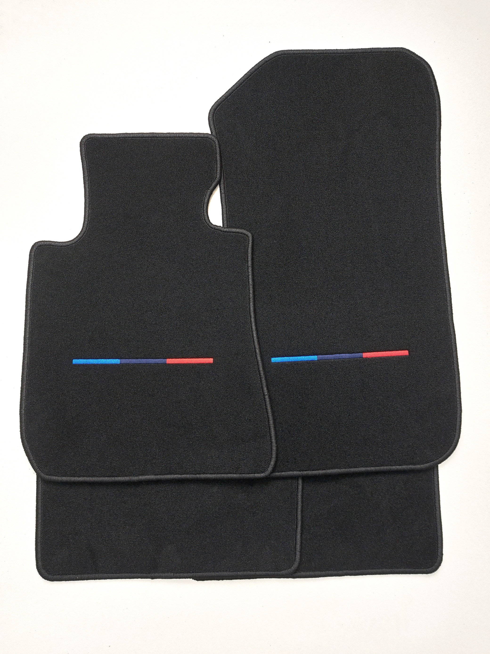 4er Set M-Farbe Vier bestickte Fussmatten für einen BMW in den M Farben mittig. Der Teppich ist schwarz.